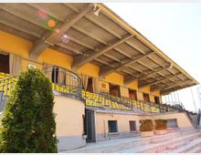 Tribuna coperta di un impianto sportivo con struttura in cemento e tetto sporgente, file di sedute gialle e ringhiere metalliche lungo il camminamento. In primo piano si vedono gradinate in cemento e alcune piante in vaso vicino all’ingresso.