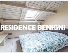 Camera da letto mansardata con soffitto in legno bianco a travi e finestra lucernario sul tetto; letto matrimoniale con copriletto a motivi floreali e pavimento in assi chiare.