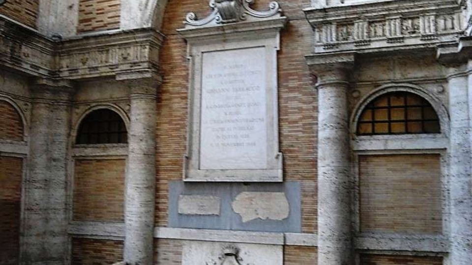 Cortile interno in stile classico con pareti in mattoni e cornici in pietra, archi e colonne laterali. Al centro c’è una lapide commemorativa incassata sotto un arco con busto scolpito, affiancata da due leoni in pietra sdraiati su basamenti su pavimentazione a mosaico.