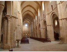 Interno di una grande chiesa in pietra con navata centrale alta, volte a crociera e arcate su robusti pilastri. Panche in legno disposte lungo la navata e rosone circolare illuminato sulla parete di fondo, con finestre strette ad arco lungo i lati.