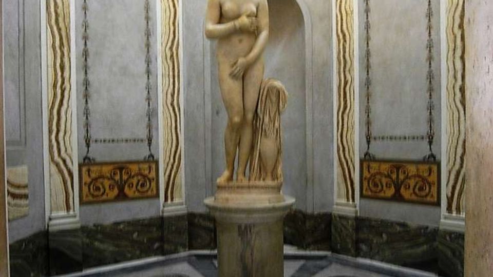Interno di una sala ottagonale in stile classico, con pareti decorate da pannelli e cornici in stucco e un soffitto a cassettoni. Al centro si trova una statua su piedistallo su un pavimento in marmo geometrico con inserti circolari.