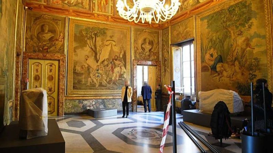 Sala storica con pareti interamente decorate da grandi affreschi e cornici dorate, soffitto ornato e grande lampadario centrale. Pavimento geometrico in marmo e alte finestre laterali, con alcuni elementi e arredi coperti o in allestimento.