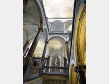 Interno di un edificio storico con grande scalone e loggiati, sorretto da alte colonne in pietra. Le volte e i soffitti sono decorati con stucchi geometrici e rosoni, con una statua in nicchia al centro del livello superiore.