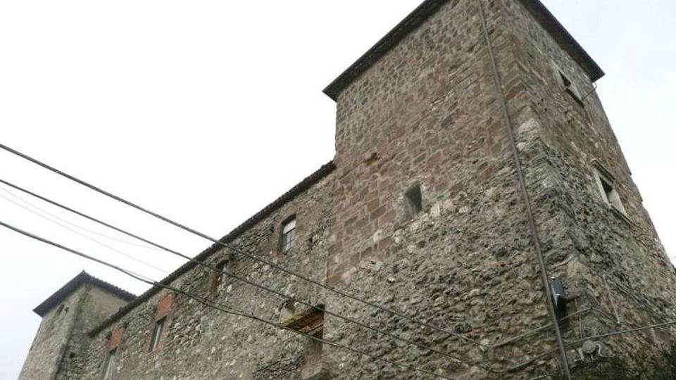 Edificio storico in pietra con due torri quadrate e piccole finestre, visto dal basso contro un cielo chiaro. Sulla facciata irregolare sono presenti cavi elettrici aerei e una gronda scura lungo il tetto.