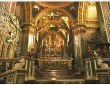 Interno di una chiesa barocca con altare rialzato e grande organo a canne sul fondo. Volte e archi riccamente dorati e affrescati, colonne decorate e balaustre in marmo ai lati.