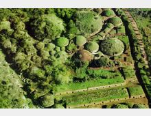 Vista aerea di un complesso immerso nel verde con numerose strutture circolari a cupola ricoperte d’erba, collegate da sentieri e muretti. Intorno si vedono alberi, aree terrazzate e un lungo muro di recinzione che delimita la zona.