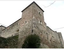 Edificio in pietra di tipo castello o palazzo fortificato, con murature massicce, piccole finestre e una torre quadrangolare sporgente. Ripreso dal basso in un contesto urbano, con un muro in pietra in primo piano e cavi aerei visibili.