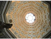 Vista verso l’alto di una cupola ottagonale decorata con motivi geometrici a cassettoni, con un lucernario poligonale centrale che lascia entrare la luce. Attorno si notano cornici e stucchi ornamentali lungo il perimetro della volta.