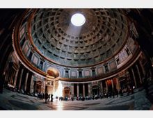 Interno di un edificio storico con grande cupola a cassettoni e oculo centrale che lascia entrare la luce. Sala circolare con colonne e nicchie lungo le pareti, pavimento in pietra e ampia apertura d’ingresso sul fondo.