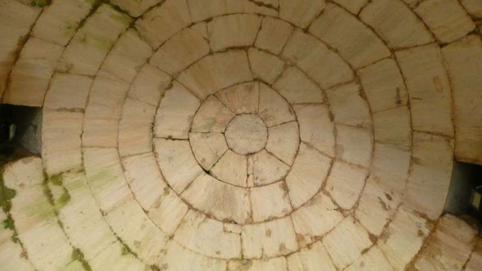 Vista dall’alto di una pavimentazione in pietra composta da lastre disposte in cerchi concentrici con un piccolo disco centrale. Le fughe tra le pietre sono visibili e in alcuni punti compare muschio.