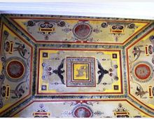 Soffitto decorato con affreschi e motivi geometrici, con cornici rettangolari e medaglioni circolari. Al centro compaiono figure di uccelli e ornamenti floreali in una composizione simmetrica dai colori ocra, rosso e blu.