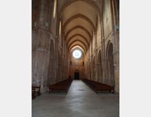 Interno di una chiesa in pietra con lunga navata centrale, arcate laterali e alte volte ogivali. In fondo si vede un grande rosone circolare sopra l’ingresso, con file di panche ai lati del corridoio.