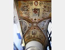 Volta a botte di un interno storico decorata con affreschi e motivi ornamentali, con riquadri centrali figurativi e cornici policrome. Ai lati si vedono lunette dipinte e una grande finestra ad arco che illumina lo spazio.