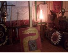 Interno di una piccola sala espositiva con scudi decorati, armature e oggetti storici disposti lungo le pareti. Sono visibili reti appese, pannelli dipinti e una luce centrale che illumina l’ambiente.