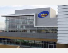 Facciata di un moderno cinema multisala con grande vetrata a pannelli e rivestimento metallico grigio, con insegna “UCI CINÉCITÉ 14 sale” sulla parte superiore. L’edificio si affaccia su una struttura commerciale con finestre continue al piano inferiore.