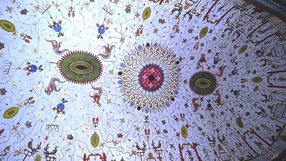Soffitto decorato con affreschi su fondo chiaro, ricco di motivi geometrici e floreali e di figure stilizzate disposte in modo radiale attorno a grandi medaglioni circolari colorati. Lungo i bordi corre una fascia ornamentale con disegni ripetuti e simboli.