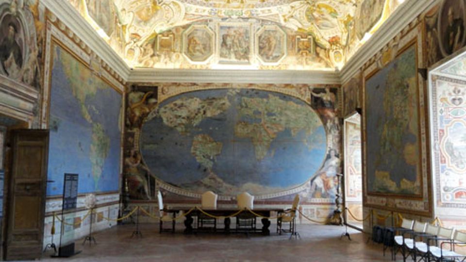 Ampia sala storica con pareti interamente affrescate con grandi mappe geografiche e decorazioni cartografiche, e un grande planisfero ovale sulla parete di fondo. Il soffitto a volta è riccamente dipinto con scene celesti e cornici ornamentali, con pavimento in cotto e file di sedie lungo un lato.
