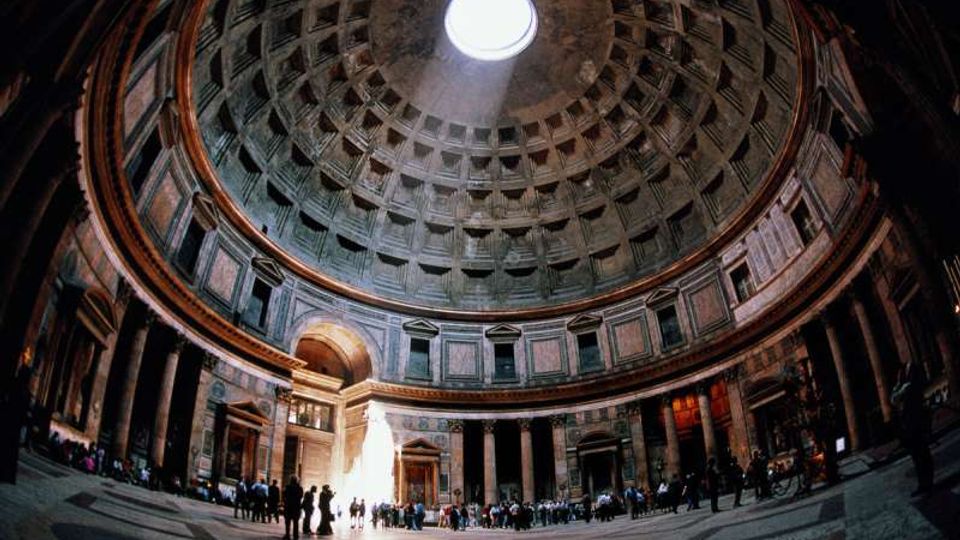 Interno di un edificio storico con grande cupola a cassettoni e oculo centrale che lascia entrare la luce. Sala circolare con colonne e nicchie lungo le pareti, pavimento in pietra e ampia apertura d’ingresso sul fondo.