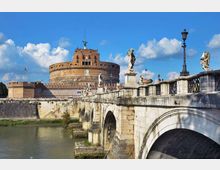 Veduta del Castel Sant’Angelo, fortezza cilindrica in mattoni, sullo sfondo, con in primo piano il Ponte Sant’Angelo in pietra ad arcate sul fiume. Sul parapetto del ponte si vedono statue, lampioni e una balaustra decorata.
