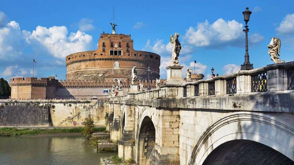Veduta del Castel Sant’Angelo, fortezza cilindrica in mattoni, sullo sfondo, con in primo piano il Ponte Sant’Angelo in pietra ad arcate sul fiume. Sul parapetto del ponte si vedono statue, lampioni e una balaustra decorata.