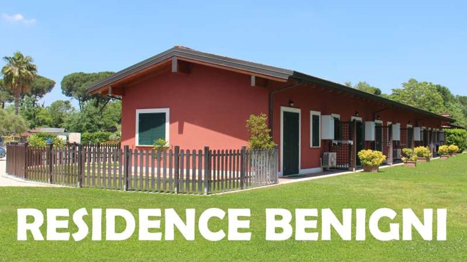 Edificio a un piano color rosso con tetto a falda sporgente, circondato da un prato verde e da una staccionata in legno. Sul fronte si vedono porte e finestre con persiane verdi, piccole verande con griglie e piante ornamentali; in basso compare la scritta “RESIDENCE BENIGNI”.