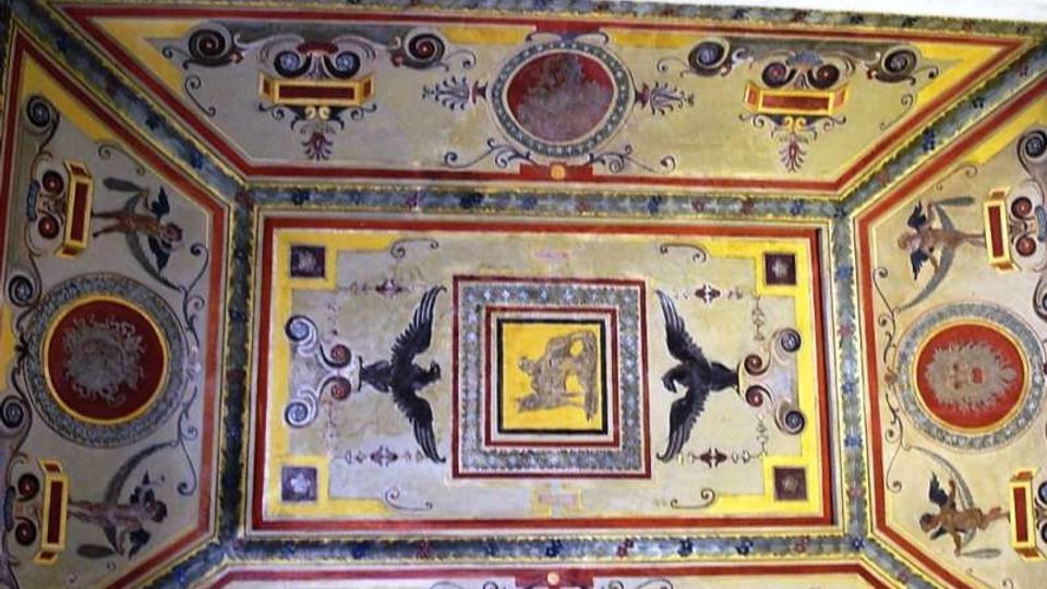 Soffitto decorato con affreschi e motivi geometrici, con cornici rettangolari e medaglioni circolari. Al centro compaiono figure di uccelli e ornamenti floreali in una composizione simmetrica dai colori ocra, rosso e blu.