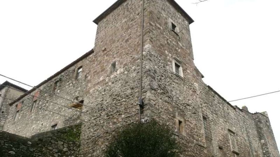 Edificio in pietra di tipo castello o palazzo fortificato, con murature massicce, piccole finestre e una torre quadrangolare sporgente. Ripreso dal basso in un contesto urbano, con un muro in pietra in primo piano e cavi aerei visibili.
