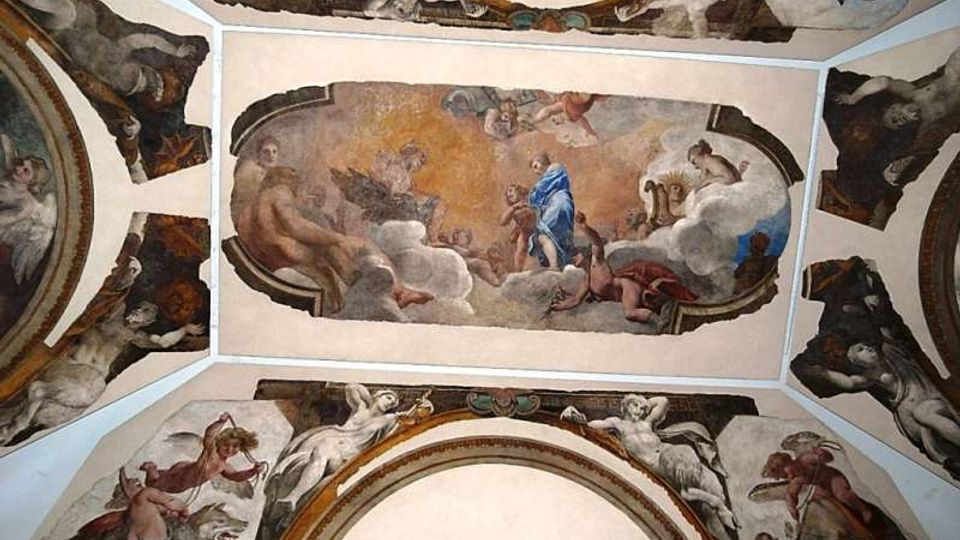 Soffitto a volta di un edificio storico decorato con affreschi, con pannello centrale rettangolare raffigurante figure tra nuvole e riquadri laterali curvi con scene allegoriche. Cornici e modanature dipinte delimitano le diverse sezioni della volta.