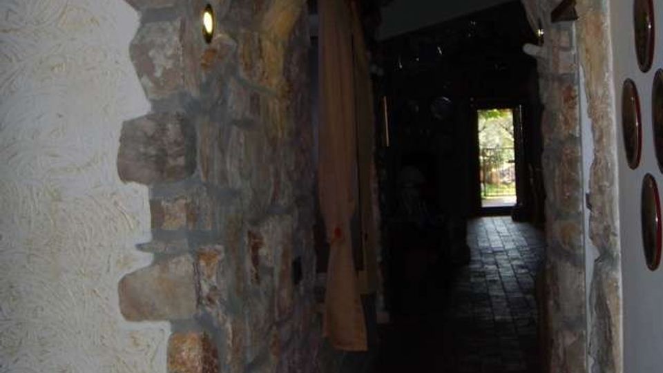 Corridoio interno stretto con arco in pietra grezza e pareti intonacate, illuminato da piccole luci a incasso. Il pavimento è in piastrelle scure e in fondo si vede una porta aperta che dà su un’area esterna luminosa.