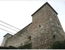 Edificio storico in pietra con due torri quadrate e piccole finestre, visto dal basso contro un cielo chiaro. Sulla facciata irregolare sono presenti cavi elettrici aerei e una gronda scura lungo il tetto.