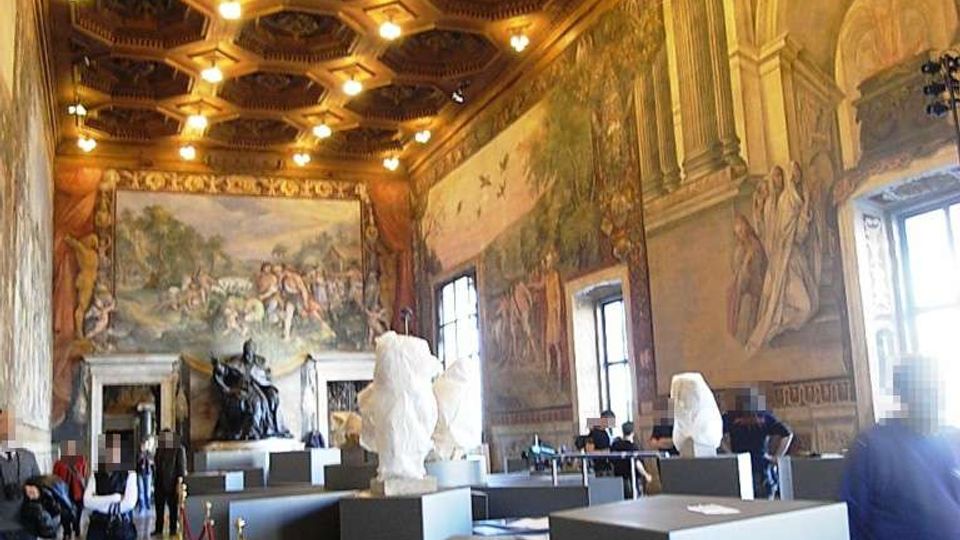 Interno di una grande sala museale con soffitto a cassettoni ottagonali illuminato e pareti affrescate con scene e architetture classiche. Nella sala sono presenti piedistalli e teche con sculture e busti, finestre alte sui lati e cordoni rossi che delimitano il percorso sul pavimento in marmo.
