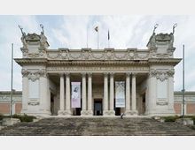 Facciata monumentale di un museo con ampio portico neoclassico sostenuto da colonne e scalinata frontale; in alto sono visibili decorazioni scultoree e bandiere. Sopra l’ingresso compare l’insegna “Galleria Nazionale d’Arte Moderna”, con grandi banner espositivi ai lati del portale.