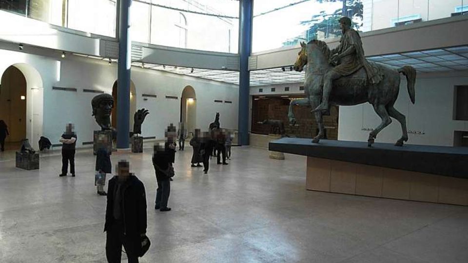 Ampio atrio museale con pavimento in pietra e soffitto vetrato sostenuto da colonne, illuminato da grandi finestre e circondato da arcate e pareti bianche. Al centro domina una grande statua equestre su basamento, con altre sculture esposte su piedistalli nella sala.