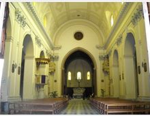 Interno di una chiesa con ampia navata centrale, file di panche in legno e soffitto a volta; ai lati si vedono arcate e decorazioni in stucco. In fondo, un grande arco introduce al presbiterio con altare e finestre ad arco illuminate.