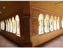 Loggiato in muratura con due file di arcate su colonne bianche, visto da un angolo interno con soffitto a volta e pavimento in cotto. Attraverso le aperture si intravedono un giardino e la luce esterna.
