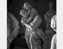 Interno di una galleria o cappella con sculture in marmo: al centro un gruppo statuario raffigurante due figure abbracciate, illuminato lateralmente, con altre statue su piedistalli sullo sfondo e pareti scure a volta.