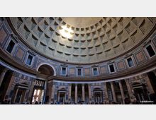 Interno di una chiesa con grande cupola a cassettoni vista dal basso, illuminata da un’apertura centrale. Sotto la cupola corre un anello di finestre e nicchie, con pareti rivestite in marmo e un colonnato che incornicia archi e cappelle laterali.