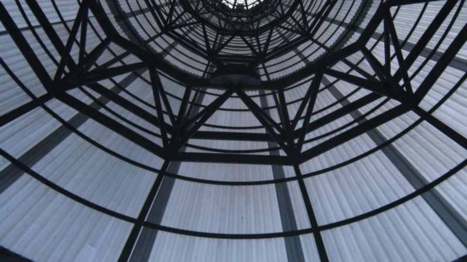 Vista dal basso di una cupola circolare in vetro e metallo, con travi nere che formano una struttura reticolare radiale. Il soffitto traslucido crea un lucernario centrale e anelli concentrici che definiscono l’architettura interna.