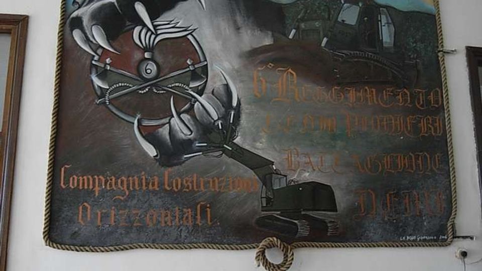 Grande murale dipinto appeso a una parete interna bianca, raffigurante una pantera nera sopra una mappa e macchinari da cantiere, con scritte decorative. Il quadro è incorniciato da una corda e montato sopra una boiserie in legno.
