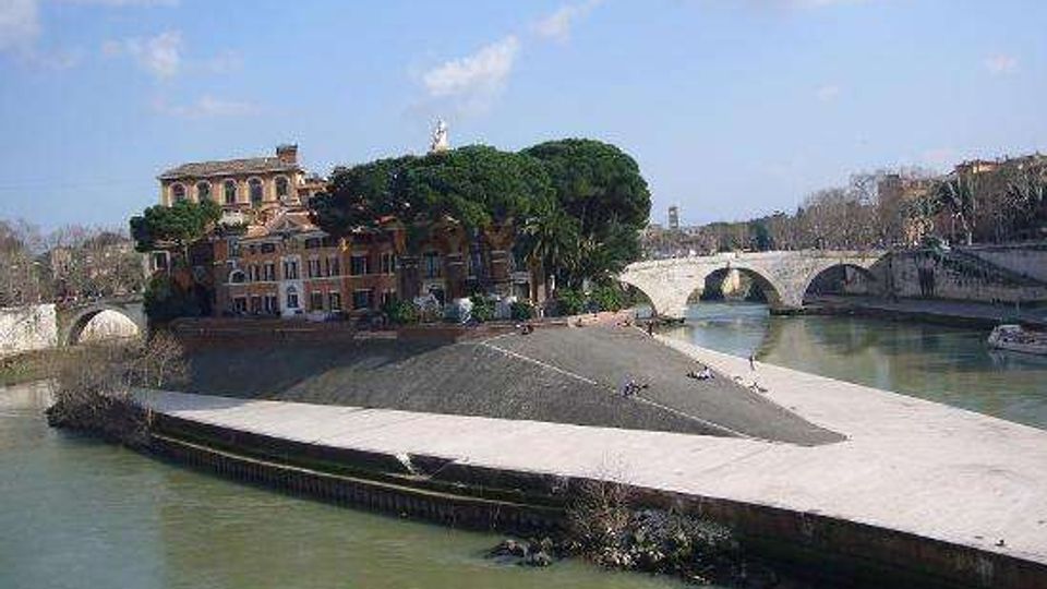 Veduta di un’isola fluviale alla confluenza di due rami del fiume, con viale alberato e edifici storici tra grandi pini. Sullo sfondo si vedono ponti in pietra ad archi che attraversano l’acqua lungo le banchine.