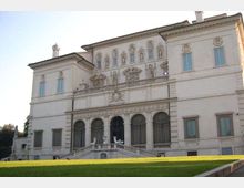 Facciata di una villa o palazzo storico in stile rinascimentale, con decorazioni a rilievo, finestre simmetriche e loggia ad archi al piano terra. Davanti si vede una scalinata con balaustra che conduce all’ingresso e un ampio prato verde in primo piano.