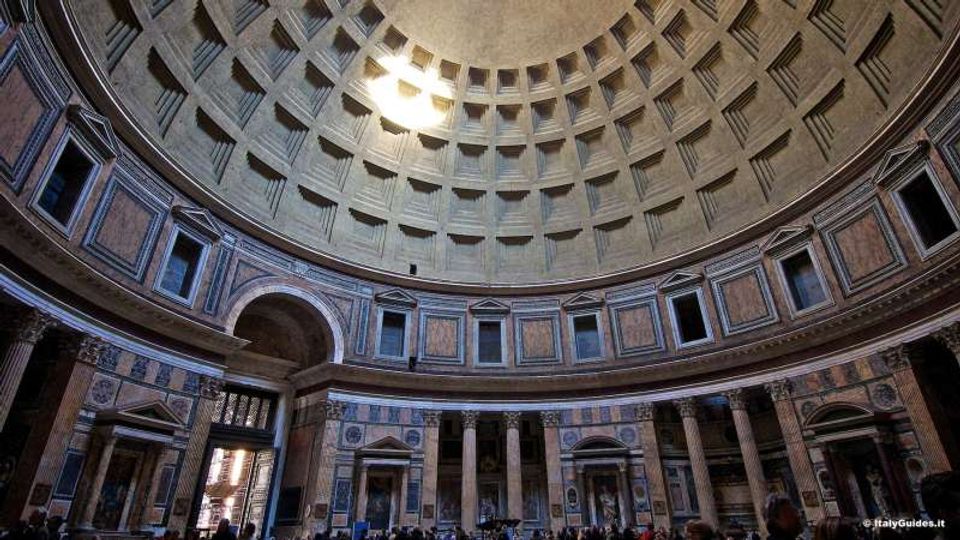 Interno di una chiesa con grande cupola a cassettoni vista dal basso, illuminata da un’apertura centrale. Sotto la cupola corre un anello di finestre e nicchie, con pareti rivestite in marmo e un colonnato che incornicia archi e cappelle laterali.