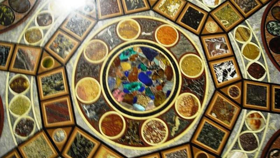 Dettaglio ravvicinato di un soffitto a cupola decorato con mosaici geometrici, con un medaglione circolare centrale in vetro colorato e anelli concentrici di riquadri e cerchi con motivi ornamentali. La superficie è suddivisa in pannelli multicolori incorniciati, con una forte luce proveniente da un lato.