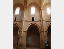 Interno di una chiesa romanica in pietra con alte arcate a tutto sesto e pilastri massicci. Finestre strette e alte nella parete superiore lasciano entrare luce naturale, con piccole aperture e pannelli informativi alla base.