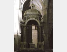 Interno di una chiesa in pietra con cappella laterale ad arco, sostenuta da colonne scure e sormontata da una cupola con piccolo lanternino. In primo piano si vede un altare semplice, incorniciato da alte volte ogivali e pareti in muratura.