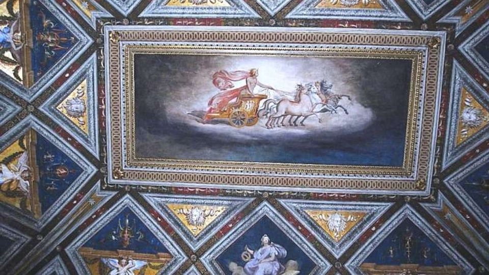 Soffitto interno riccamente affrescato con pannelli geometrici a rombi e triangoli, decorati con figure e motivi ornamentali. Al centro, un grande riquadro dipinto raffigura un carro trainato da cavalli, incorniciato da bordi dorati.