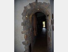 Corridoio interno stretto con arco in pietra grezza e pareti intonacate, illuminato da piccole luci a incasso. Il pavimento è in piastrelle scure e in fondo si vede una porta aperta che dà su un’area esterna luminosa.