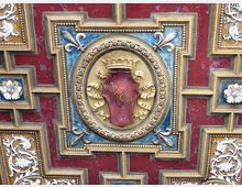 Dettaglio ravvicinato di una decorazione architettonica a soffitto con motivo geometrico rosso e blu, cornici dorate e ornamenti in stucco bianco. Al centro, un medaglione circolare con stemma dorato e la scritta “SPQR” su fondo rosso.