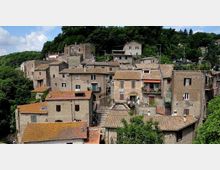 Borgo collinare con case in pietra addossate tra loro e tetti in coppi, disposte su più livelli con scalinate e piccoli balconi. Sullo sfondo una fitta area boschiva circonda l’abitato.