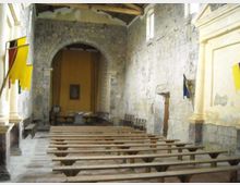 Interno di una piccola chiesa in pietra con navata semplice, file di panche in legno e grande arco che conduce all’area dell’altare sul fondo. Pareti in muratura a vista, finestre alte e soffitto con travi lignee.